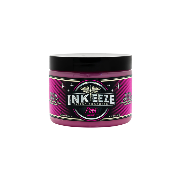 Un pot d'INK-EEZE Pink Glide - Baume pour tatouage multi-usage avec un couvercle noir et une étiquette rose, noire et verte représentant des ailes et des étoiles, sur fond blanc.